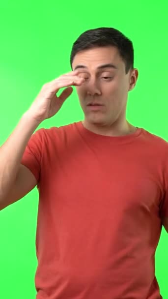 Kerl im roten T-Shirt berührt Stirn und winkenden Arm bei starkem Ohnmachtsanfall gegen Chromakey im Studio - Filmmaterial, Video