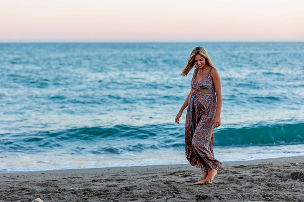 Una joven embarazada feliz con un vestido caminando en la orilla del mar - Foto, imagen