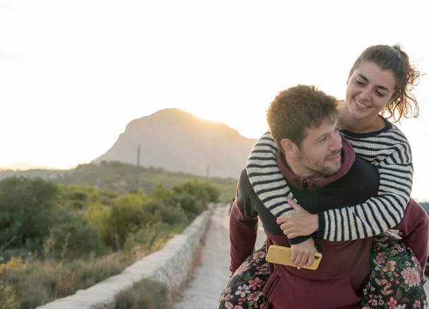 A couple in piggyback looking at the horizon during sunset - Foto, Imagen