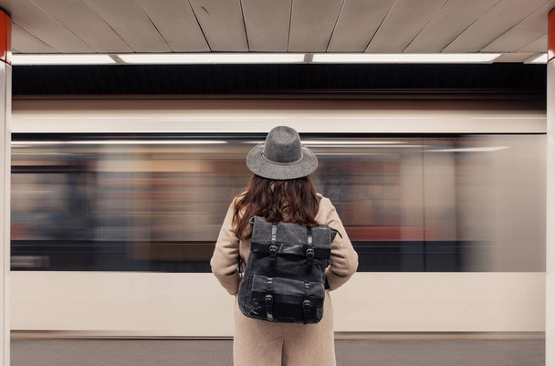 Rear view of woman standing on subway platform in front of moving train. - Foto, Bild