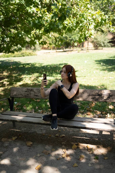 A girl using a smartphone and listening music in headphones on a sunny summer day in a park - 写真・画像