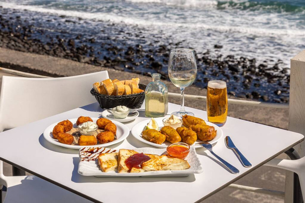 A close-up shot of fried fast food and French toast on a white table with a background of a beach - Fotó, kép