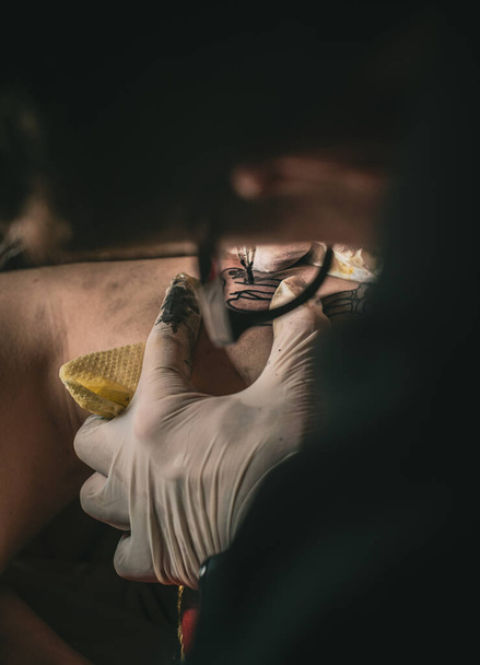 primer plano de una pistola de tatuaje y el proceso de aplicación del tatuaje en la piel de una persona - Foto, Imagen