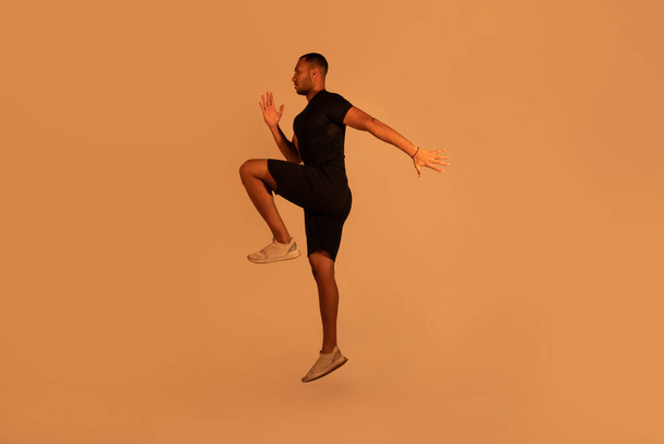 Визначений чорний фітнес хлопець вправляється, роблячи лікоть для коліна розбивається або стрибає позуючи над бежевим студійним фоном, повнометражний знімок. Здоровий спосіб життя, спорт та концепція тренування
 - Фото, зображення