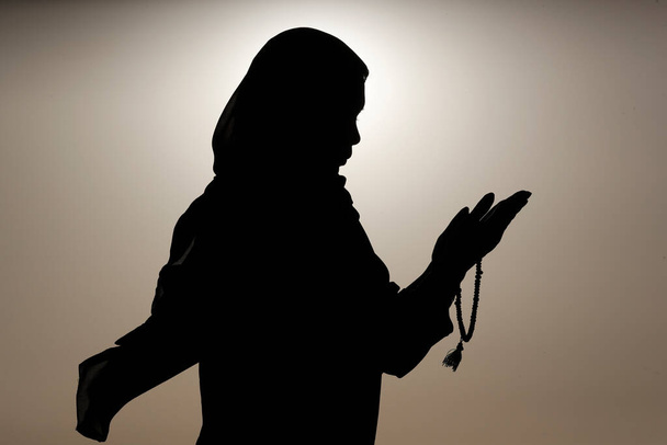 Sylwetka muzułmanki trzymającej w rękach paciorki modlitewne i modlącej się o niebo. Koncepcja modlitwy religijnej - Zdjęcie, obraz
