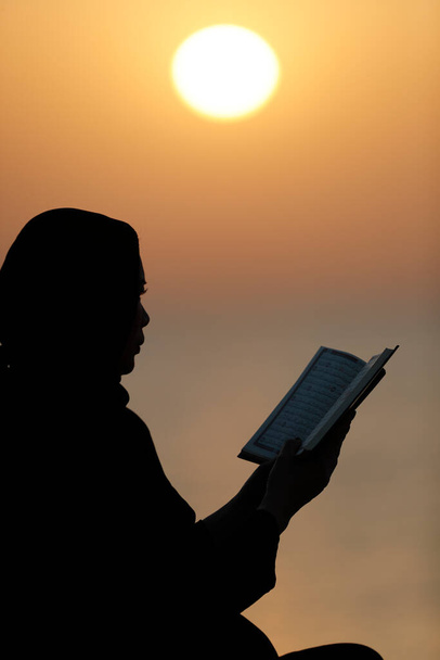 Silueta de mujer musulmana leyendo el Noble Corán al atardecer. Concepto de oración religiosa. Emiratos Árabes Unidos - Foto, imagen