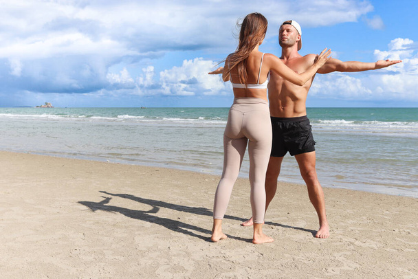 Δύο φίλε κάνει ασκήσεις τεντώματος σώματος εξωτερική για το καλοκαίρι τροπικό νησί παραλία με μπλε θάλασσα, ζευγάρι κάνει άσκηση εξωτερική, ο αθλητισμός άνθρωπος και η γυναίκα αθλητής εραστής κάνει και προπόνηση προπόνηση στην παραλία. - Φωτογραφία, εικόνα