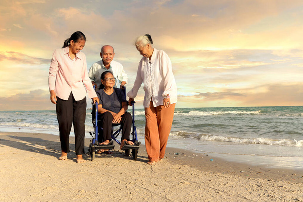 Група з чотирьох веселих літніх людей мають поїздку на відкритому повітрі разом, щасливі інваліди старшої жінки в інвалідному візку подорожують з друзями на пляжі заходу сонця, насолоджуються проведенням часу у відпустці
. - Фото, зображення