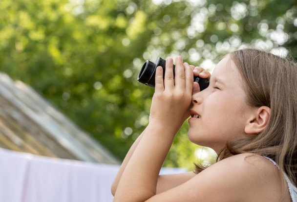 Elementary school age girl looking up into the sky through a magnifying monocular glass, finding, searching for something. Copy space, blurred background. Advertisement eyeing deals, discounts concept - Photo, Image