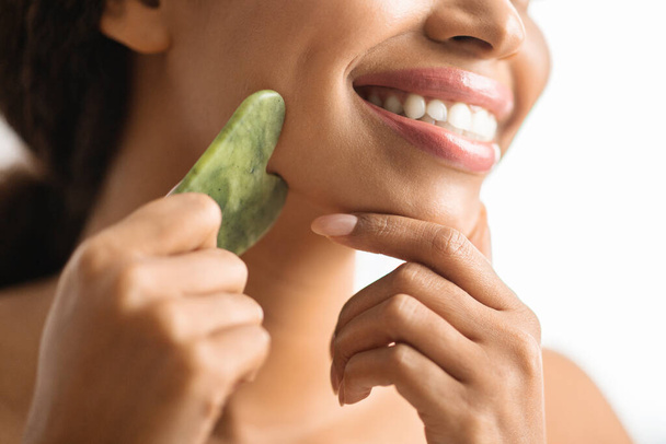 Smiling Black Woman Making Lifting Face Massage With Gua Sha Stone Scraper At Home, Closeup Shot Of Attractive Young African American Female Doing Anti-Aging Skincare Routine, Cropped - Фото, зображення
