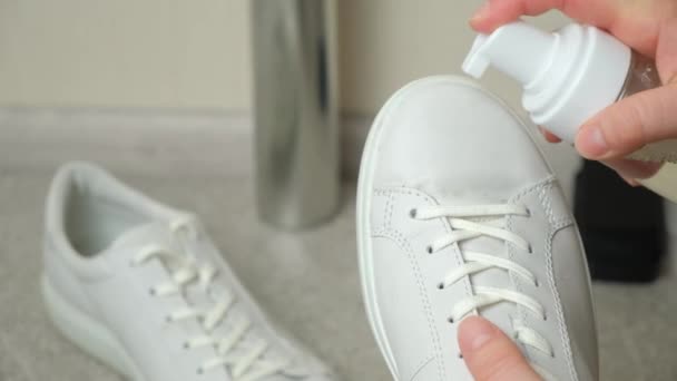 Aplicando espuma limpiadora de la botella a las zapatillas de deporte para mujer de cuero blanco. Cuidado de los zapatos de cuero, blanqueamiento de superficies. - Imágenes, Vídeo