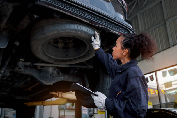 ガレージで美しい女性の自動車整備士チェックホイールタイヤ,車サービス技術者女性は、自動車サービスで顧客の車を修復します,車両の車体とサスペンションエンジンシステムを検査. - 写真・画像