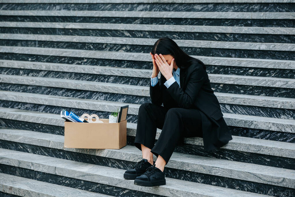 An anxious woman sits on cardboard boxes on the steps, feeling the insecurity and uncertainty of her. Caucasian Female Looking Desperate on Steps - Foto, afbeelding