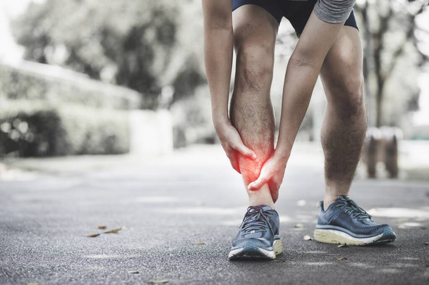 Fitness injury concept: Asian man holding his ankle while running on the street in the park. - Foto, Bild