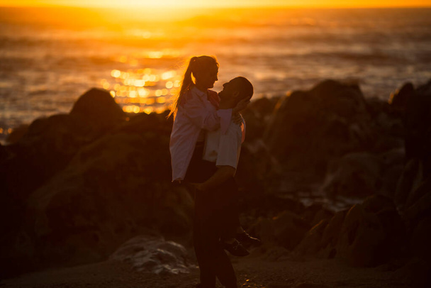 Una giovane coppia innamorata che si diverte sull'oceano durante un tramonto dorato. - Foto, immagini