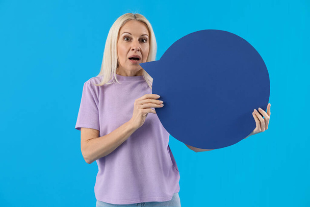 Mature woman with blank speech bubble on blue background - Foto, afbeelding