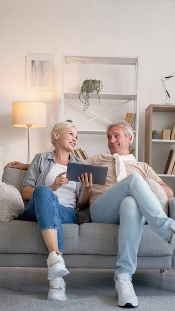 Family leisure. Happy couple. Online movie. Smiling middle-aged man and woman sitting sofa with laptop in light home interior. - Photo, image