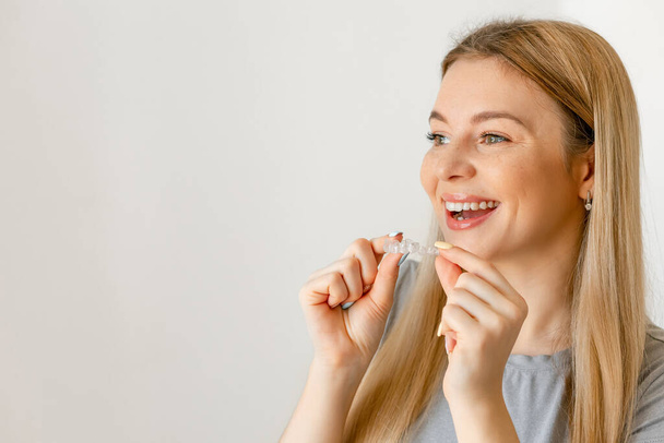 Concepto de Tratamiento Dental. Primer plano de mujer con sonrisa perfecta sosteniendo alineador invisible, bandeja de blanqueamiento, espacio libre - Foto, imagen