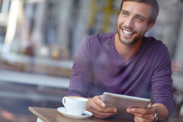 Aan het chillen in zijn plaatselijke café. een knappe jongeman die er attent uitziet terwijl hij met zijn tablet in een koffiehuis zit - Foto, afbeelding