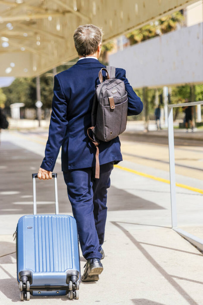 Элегантный бизнесмен проверяет электронную почту на мобильном телефоне во время прогулки с чемоданом внутри аэропорта - Фото, изображение