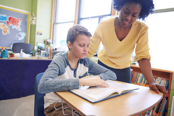 A gyakorlás nem teszi tökéletessé a fejlődést. Egy fiatal tanár segít egy diáknak az íróasztalánál. - Fotó, kép