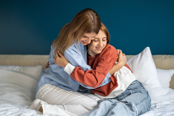 Blij lachende tiener meisje knuffelen omarmen moeder tonen liefde dankbaarheid genegenheid nauwe goede relatie. Ouder vrouw en dochter brengen tijd samen door thuis voelen zich beschermd tegen problemen. - Foto, afbeelding