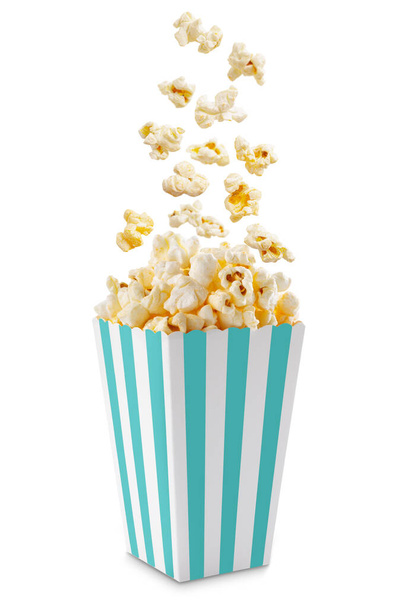 Popcorn fliegt aus einer türkis-weiß gestreiften Pappschachtel, isoliert auf weißem Hintergrund mit Kopierraum. Splash, Schweben von Popcornkörnern.  - Foto, Bild