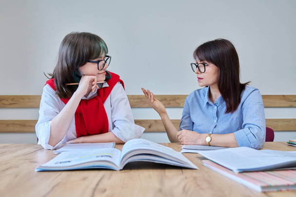 Young teenage female studying foreign languages in course with teacher. Tutor and student sitting at desk in office, using books, notebooks. Education, knowledge, learning concept - Fotografie, Obrázek
