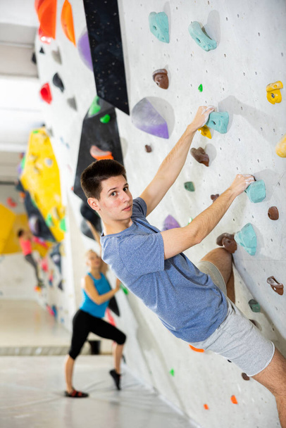 European young man grabbing ledges of artificial climbing wall in bouldering centre. - Foto, immagini
