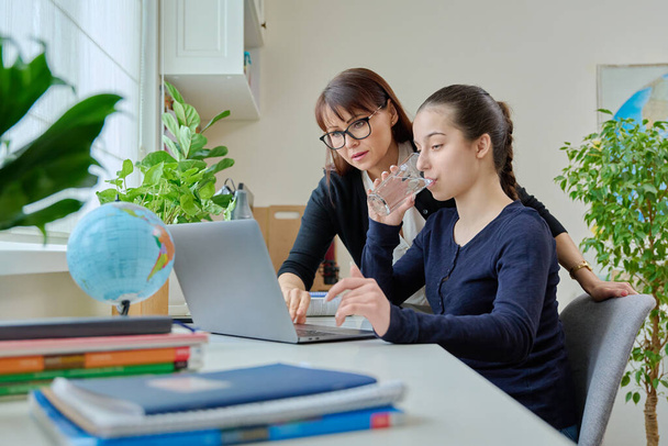 Teenage girl studying, female teacher with textbook helps, tells, teaches, tests the level of knowledge. Mentor, school counselor together with student preparing scientific work. Education adolescence - Zdjęcie, obraz
