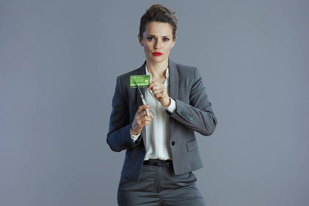 estressado jovem empresário mulher em terno cinza com cartão de crédito e tesoura isolada em fundo cinza. - Foto, Imagem