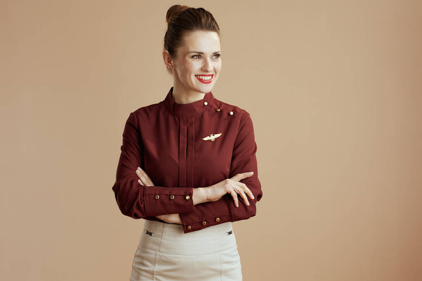 happy stylish female flight attendant on beige background looking at copy space. - Foto, afbeelding