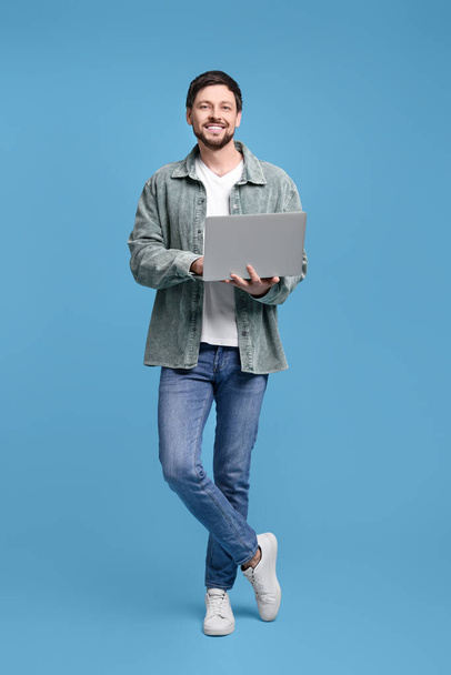Happy man with laptop on light blue background - Fotoğraf, Görsel