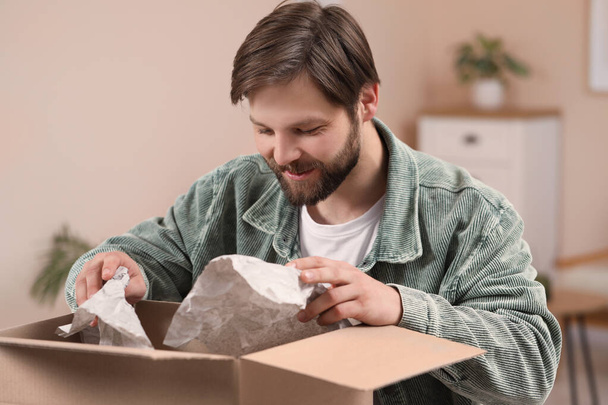 Happy man opening parcel at home. Internet shopping - 写真・画像