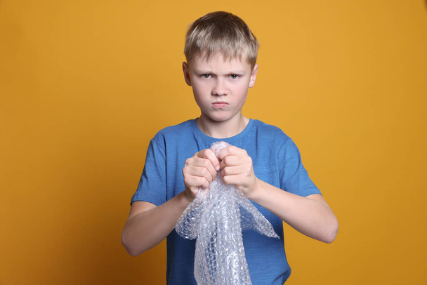 Angry boy popping bubble wrap on yellow background. Stress relief - Zdjęcie, obraz