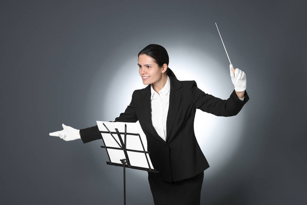 Happy professional conductor with baton and note stand on grey background - Foto, Imagen