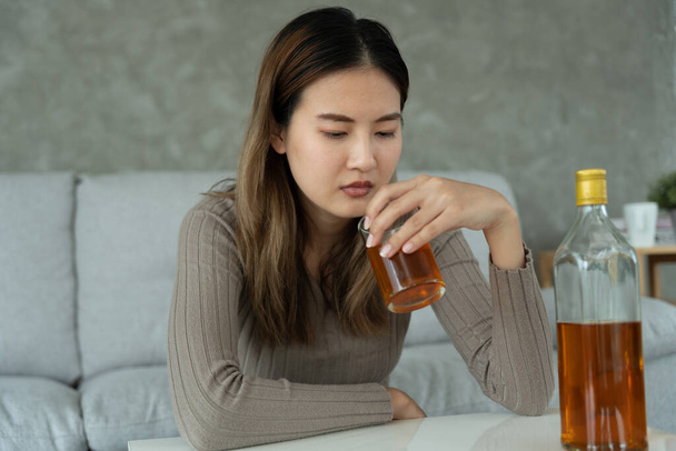 Depressed young Asian woman addicted feeling bad drinking whiskey alone at home, stressed frustrated lonely drinking alcohol suffers from problematic liquor, alcoholism, life and family problems - Foto, afbeelding