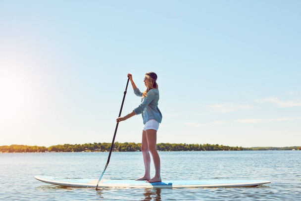 It makes her feel calm. an attractive young woman paddle boarding on a lake - Фото, изображение