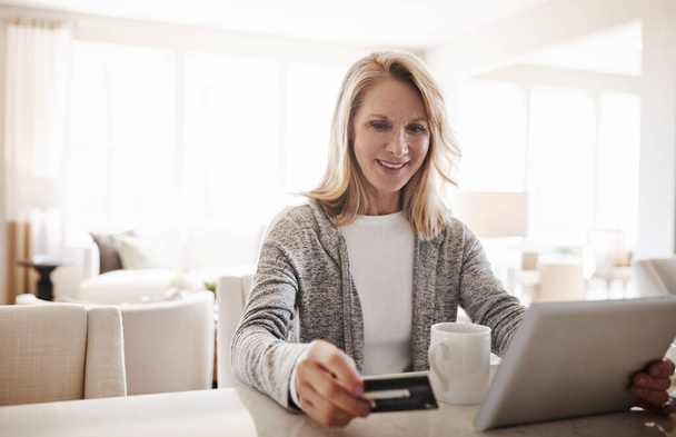 Anything I need whenever I need it. a mature woman using a credit card and digital tablet while relaxing at home - Foto, Imagem