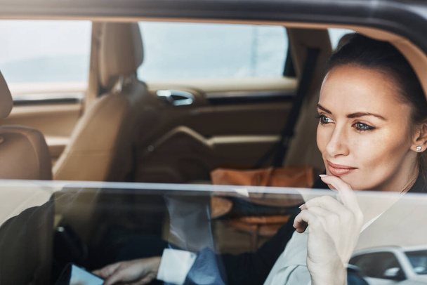 Mirando hacia las calles ocupadas. una joven empresaria confiada sentada en un coche como pasajero mientras estaba ocupada en su teléfono y mirando por la ventana - Foto, Imagen