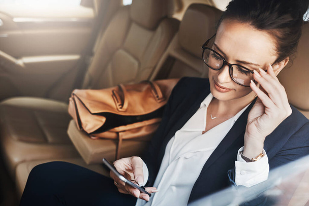 Άλλη μια εργάσιμη μέρα. μια σίγουρη νεαρή επιχειρηματίας που κάθεται σε ένα αυτοκίνητο ως επιβάτης ενώ στέλνει μηνύματα στο τηλέφωνό της στο δρόμο για τη δουλειά της - Φωτογραφία, εικόνα