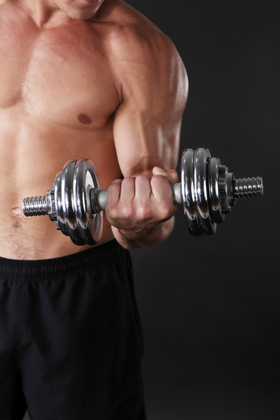 Muscle young sportsman execute exercise with dumbbell on dark background - Φωτογραφία, εικόνα