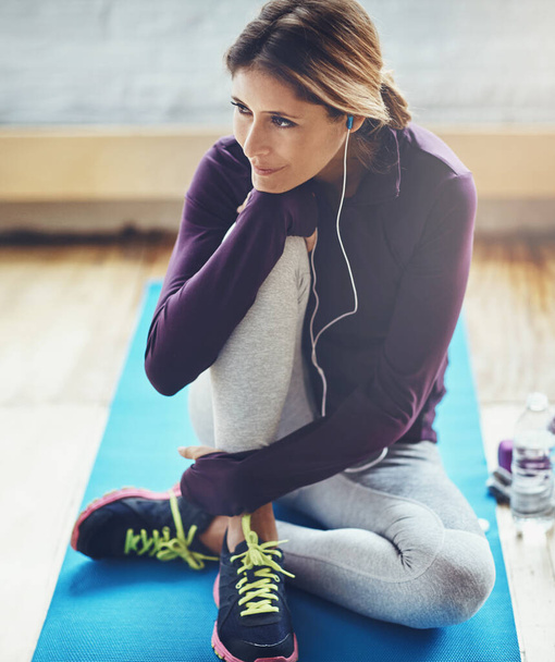 Fitness leidt tot geluk. een aantrekkelijke jonge vrouw luisteren naar muziek tijdens het sporten thuis - Foto, afbeelding