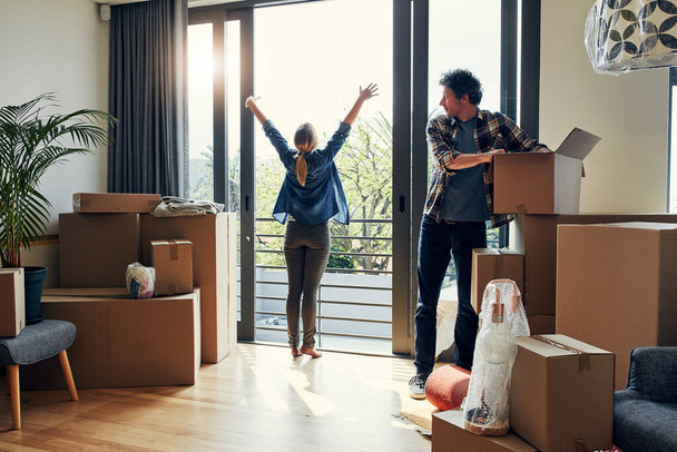 Hello there neighbors. a cheerful middle aged woman stretching her arms out on her balcony while her husband looks at her and packs out boxes on moving day - Foto, imagen