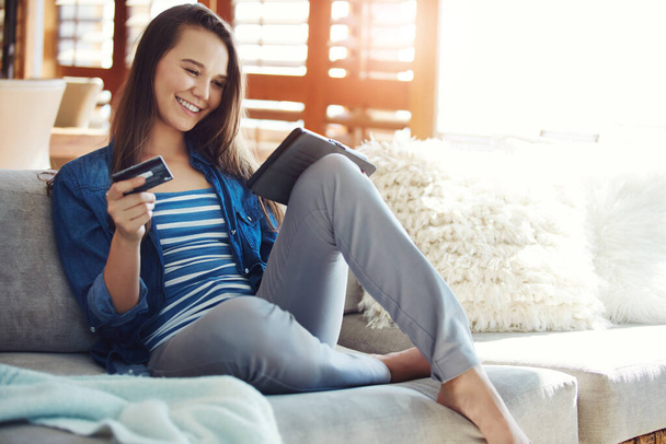 Technologie macht alles so bequem. eine attraktive junge Frau kauft mit ihrem Tablet online ein, während sie es sich zu Hause auf dem Sofa gemütlich macht - Foto, Bild