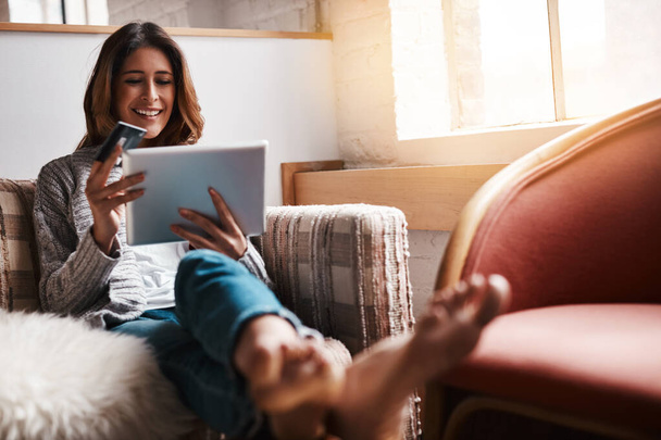 Settled in for a bit of virtual shopping. an attractive young woman using a digital tablet and credit card on the sofa at home - Foto, afbeelding