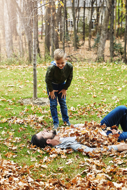 All you hear are giggles amongst the golden leaves. a father and his little son playing in the autumn leaves outdoors - Foto, afbeelding