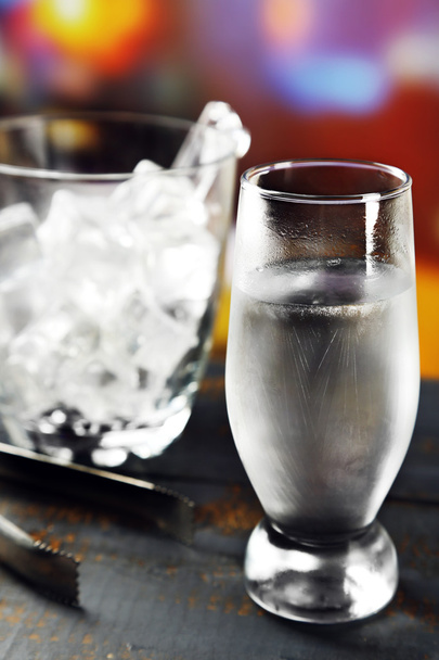 Glass of water with ice on wooden table and bright blurred background - Valokuva, kuva