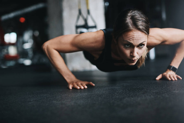 Nothing stops her. Nothing. an attractive young woman doing push ups in a gym - Фото, зображення