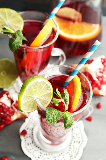 Pomegranate drink in glasses with mint and slices of orange and lime on color wooden background - Photo, Image